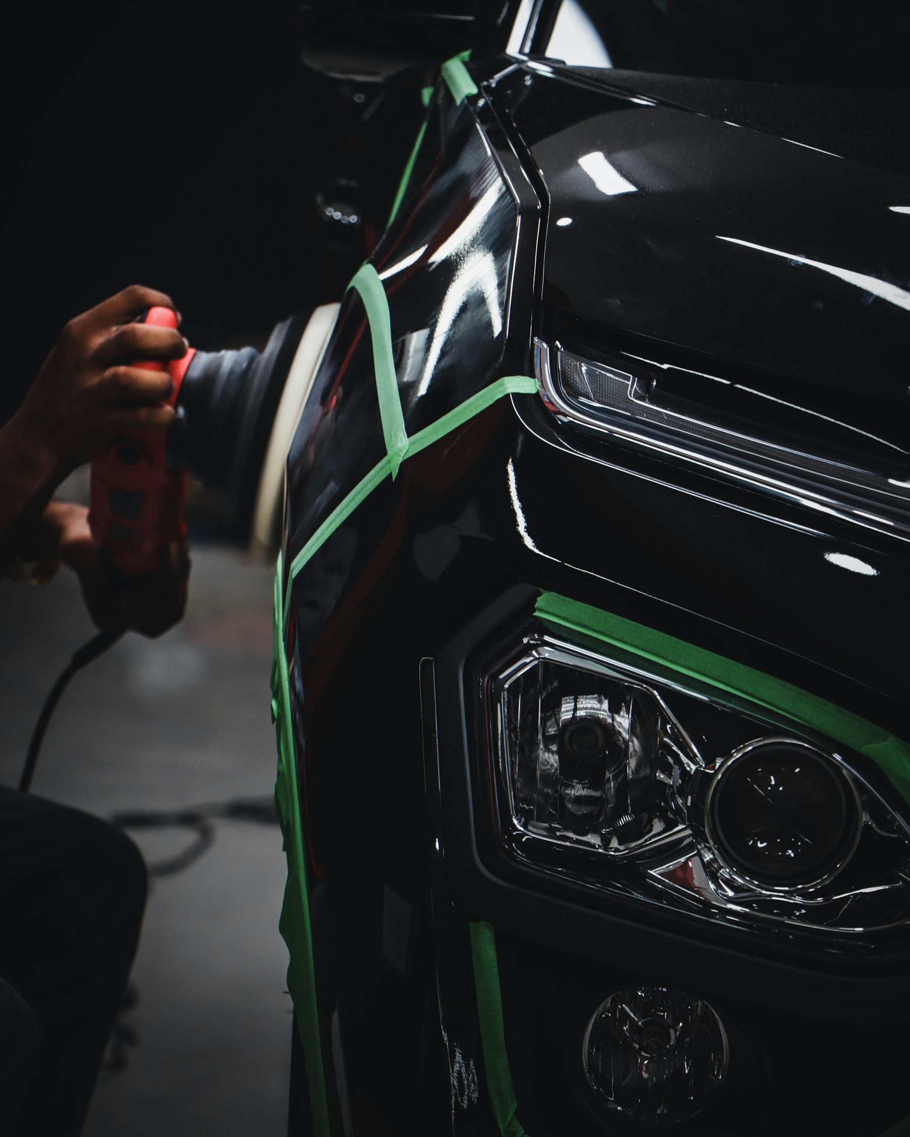 Automotive detailer polishing a black vehicle beside its headlight